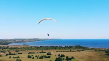 Bir adam tarlaların üzerinde planörle gökyüzünde uçuyor..