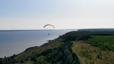 Bir adam nehir kenarında planörle uçuyor..