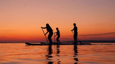 Gençler paddleboards üzerinde sunset gölü geçiyor