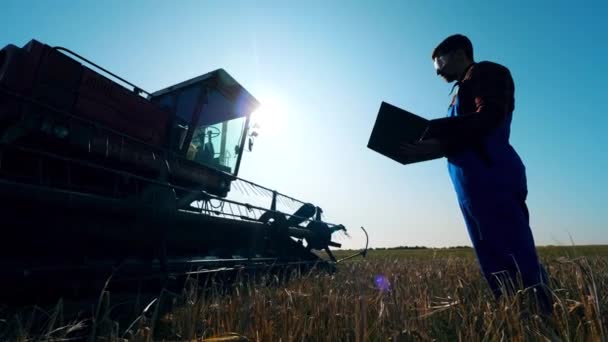 Granjero comprueba tractor en un campo, trabajando con el ordenador portátil. Agricultor en un campo agrícola . — Vídeos de Stock