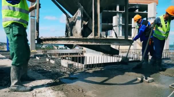 Dělníci vylévají beton na podlahu a vyrovnávají ho. — Stock video