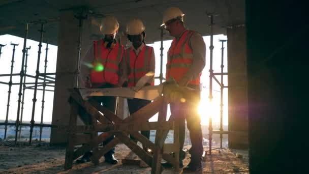 Bouwvakkers op moderne bouwplaats. Glimlachende ingenieurs kijken naar een blauwdruk op een bouwplaats. — Stockvideo