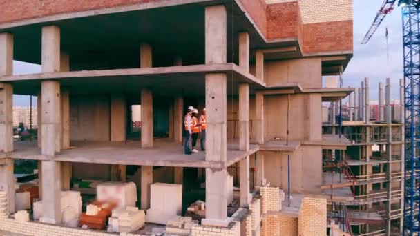 Trzech budowniczych omawia pracę, stojąc w niedokończonym domu. — Wideo stockowe