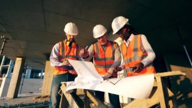 Üç işçi bir inşaat alanının planına bakıyor. Modern şantiyede inşaat işçileri.