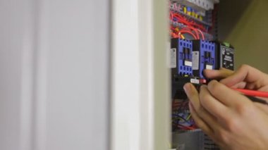Elektrikçi elektriği test ediyor. Sanayi fabrikası elektrikçisi elektrik kalkanında çoklu metre kullanarak voltajı test ediyor..