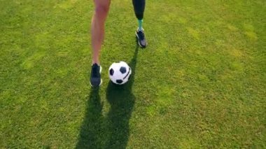 Futbol oynayan fiziksel engelli bir adamla yeşil çimenlik.