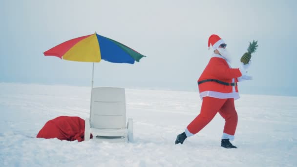 Cheerful Santa Claus is dancing with a pineapple next to a deck-chair — Stock Video