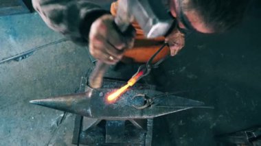 Demircinin biri çekiçle örse bıçak şekli veriyor..