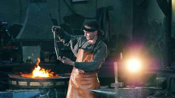 Un forgeron vérifie un couteau, le tenant dans ses mains . — Video