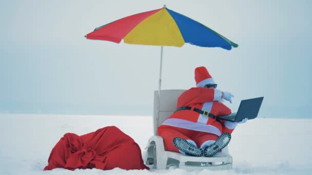 Snowy landscape with Santa Claus in a deck-chair making a videocall — Stock Video