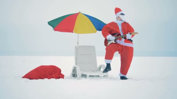Papai Noel está tocando guitarra ao lado de sua cadeira de praia — Vídeo de Stock