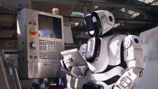 Biały cyborg pracuje z tabletem, sprawdzając maszynę fabryczną. — Wideo stockowe