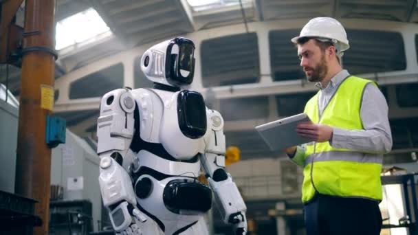 Un ingegnere controlla un androide funzionante, utilizzando un tablet . — Video Stock