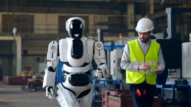 Trabajador de fábrica comprueba un cyborg caminando, usando una tableta . — Vídeos de Stock
