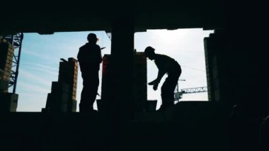 Arkadan ışıklandırılmış taş işçileri bir duvar örüyor.
