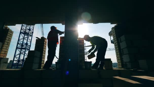 Construção da parede de tijolo feita por construtores retroiluminados — Vídeo de Stock
