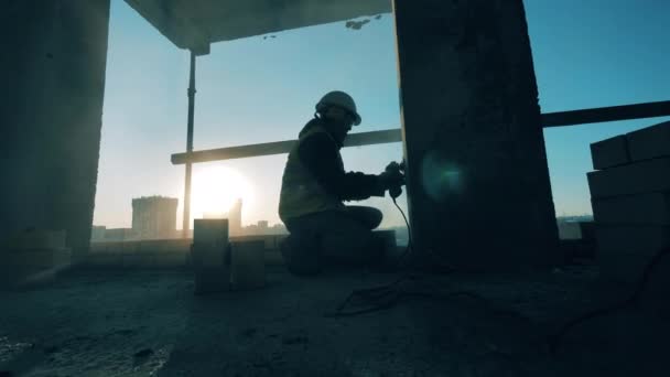 Pracovník v uniformě brousí zeď na pozadí západu slunce.