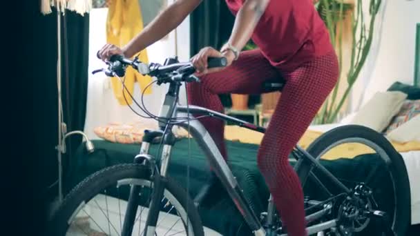 Mujer afroamericana está entrenando en bicicleta estática en casa durante la cuarentena . — Vídeos de Stock