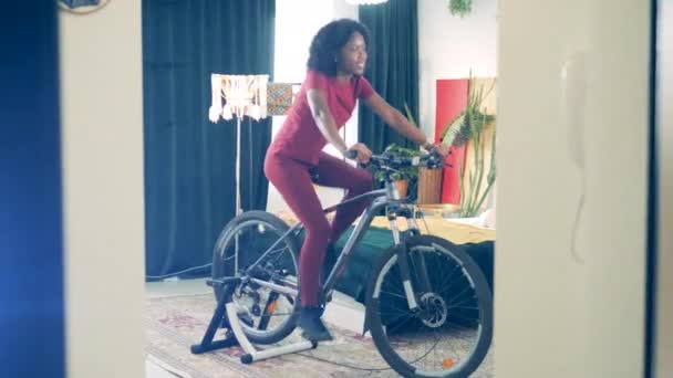 Mujer sonriente usa bicicleta estática mientras se queda en casa en cuarentena . — Vídeo de stock