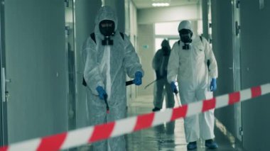 Üç işçi sterilize etmek için koridoru spreyliyor..