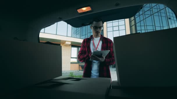 Zusteller kontrolliert Pakete im Kofferraum eines Autos — Stockvideo