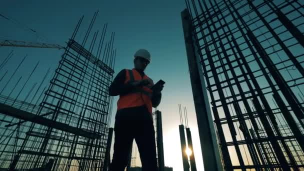 İnşaat endüstrisi, inşaat projesi, gün batımında inşaat süreci. Hesaplamalar yapan bir erkek mühendis ile günbatımı inşaatı — Stok video