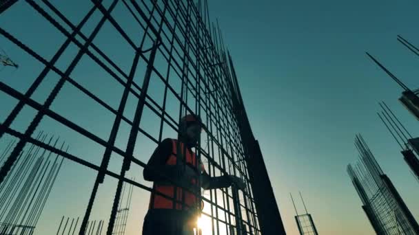 Építőipar, építési projekt, építési folyamat naplementekor. A munkás egy fémvázat állít össze a tetőn naplementekor. — Stock videók