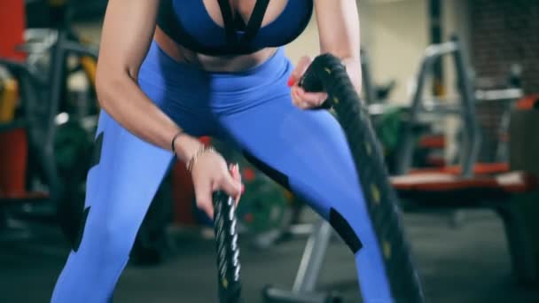 Una mujer entrena con cuerdas de batalla en el gimnasio . — Vídeos de Stock