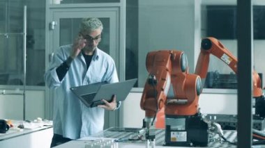 Bilgisayar uzmanı nesneleri değiştiren bir robotik kol gözlemliyor