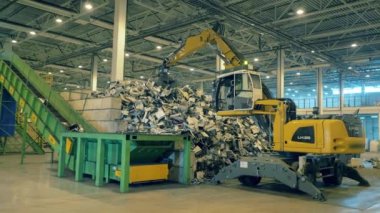 Sarı kazıcı bir fabrikadaki konveyöre çöp koyuyor. Geri dönüşüm süreci, plastik ikincil kullanımı.