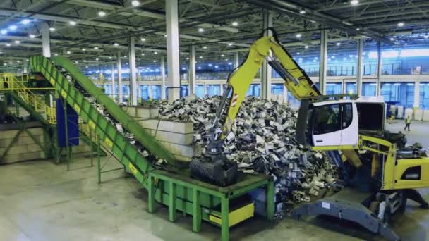 Prullenbak, e-waste, elektronische afval recyclingfabriek. Backhoe trekker verplaatst afval op transportband in een fabriek. — Stockvideo