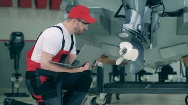 Dizüstü bilgisayarı olan tamirci tekne motorlarını kontrol ediyor.