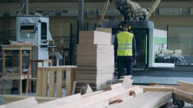 İnsanlar fabrikada kerestelerle çalışan endüstriyel makineleri izliyor..