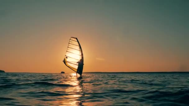 Havsvatten vid solnedgången och en man som vindsurfar i dem — Stockvideo