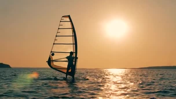 Ένας άντρας κάνει σέρφινγκ στη θάλασσα το ηλιοβασίλεμα. — Αρχείο Βίντεο