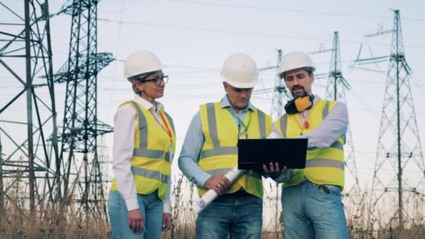 Energiearbeiders plannen een project in de buurt van elektriciteitstorens. Ingenieurs van Enrgy inspecteren een hoogspanningslijn. — Stockvideo