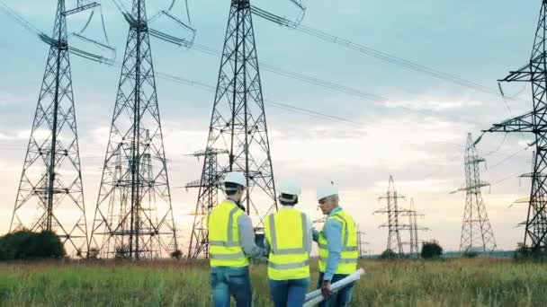 Power engineers lopen langs het veld met elektrische torens — Stockvideo