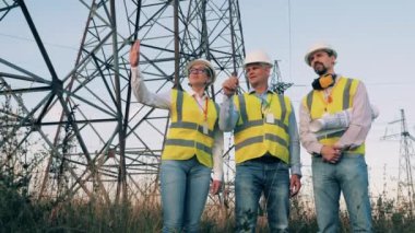 Elektrik mühendisleri elektrik kulelerinin yanında durup konuşuyorlar.