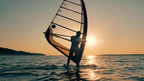 Un hombre está manejando un velero mientras flota al atardecer. — Vídeos de Stock