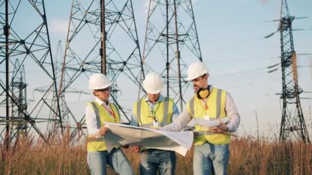 Ingenieure gehen in die Nähe von Strommasten und diskutieren ein Layout — Stockvideo