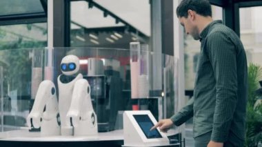 Bir adam kahve sipariş ediyor ve bir robot ona servis yapıyor.