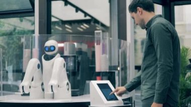 Bir adam kahve sipariş ediyor ve bir robot ona servis yapıyor.