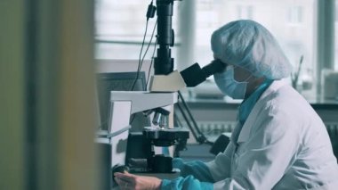 Kadın işçi mikroskop altında bir kapsül hapı keşfediyor.