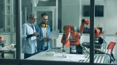 İki adam laboratuvarda robot makineleri kontrol ediyor..