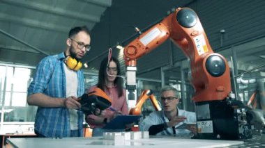 İnsanlar robotik kolu tabletlerle kontrol ediyorlar. Yenilik, yüksek teknoloji eğitimi, bilim eğitimi kavramı.