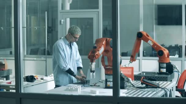 Un hombre usa un portátil para controlar el brazo robótico. Laboratorio de ciencia moderna. — Vídeos de Stock