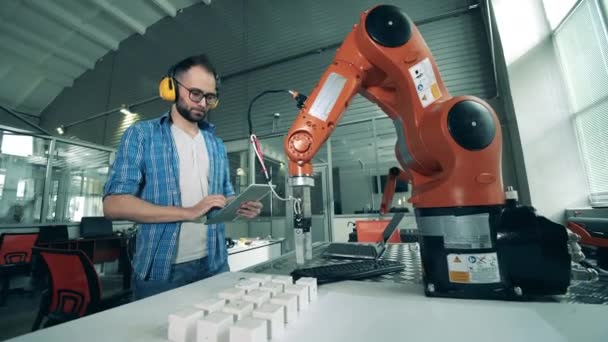 Man ingenieur controleert robotarm die blokjes beweegt. — Stockvideo