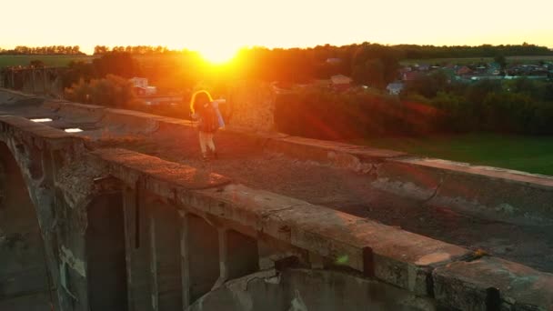 Seorang wanita berjalan di sepanjang jembatan saat matahari terbenam. Turis, perjalanan, konsep petualangan. — Stok Video