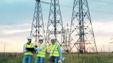 Üç mühendis olay yerindeki elektrik hatlarının yanında yürüyor. Elektrik endüstrisi, elektrik enerjisi üretim konsepti.