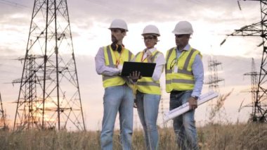 Erkekler ve kadınlar elektrik şebekeleri olan bir alanda çalışırken konuşurlar..